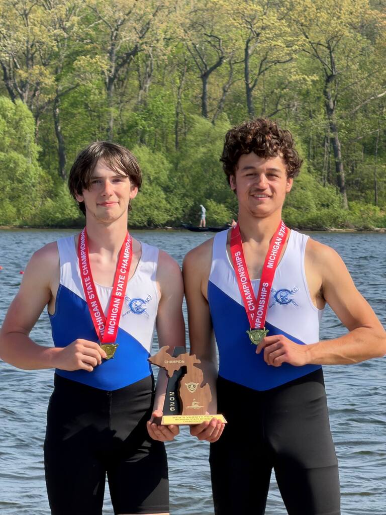 Two male rowers holding a trophy near the water