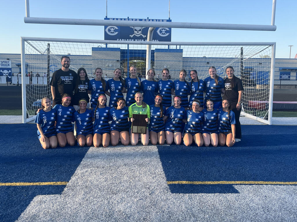 Girls soccer team and coaches posing with trophy in front of a soccer net