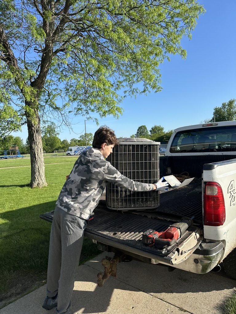 A student is standing at the back of a truck demonstrating how to break down an AC unit for scrap