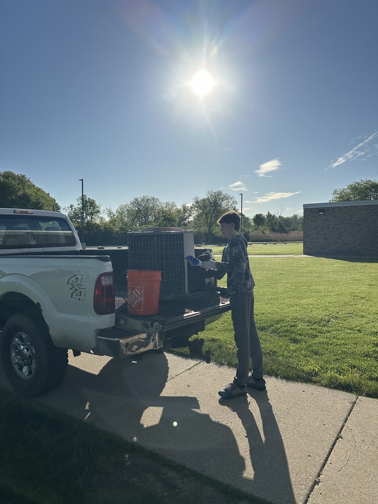 A student is standing at the back of a truck demonstrating how to break down an AC unit for scrap