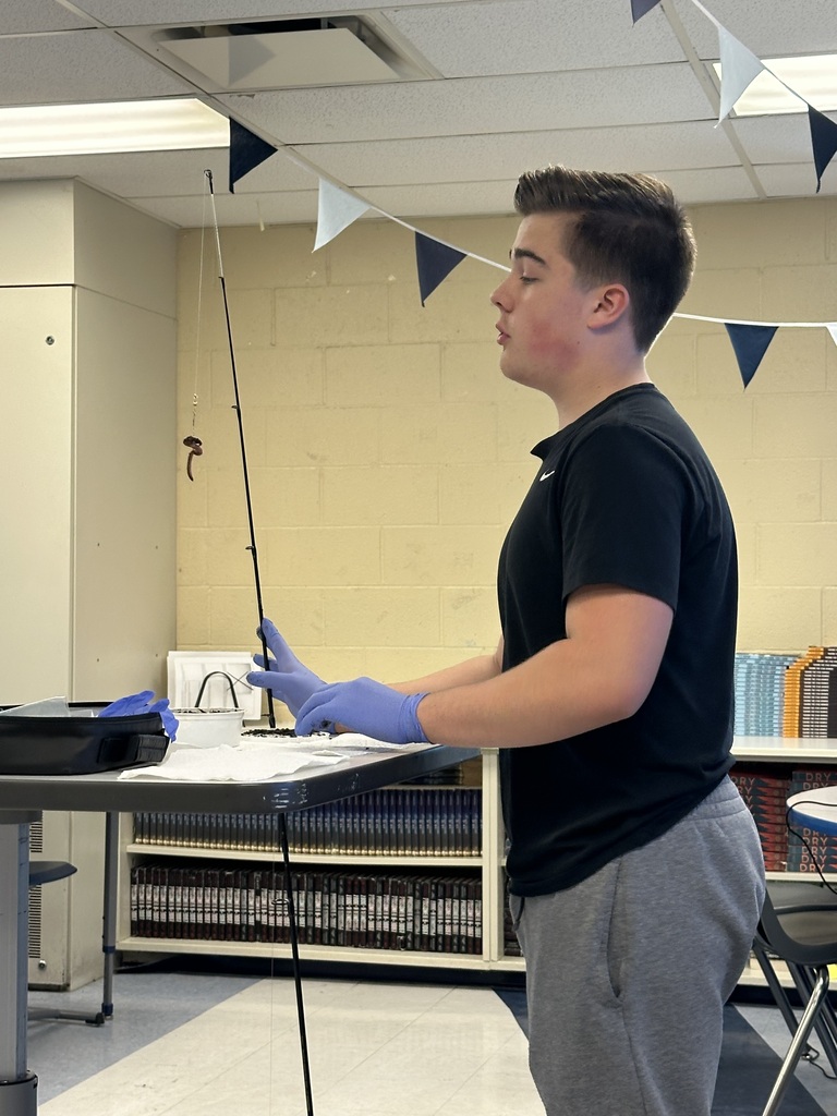 A student standing up with a fishing pole demonstrating how to use it 
