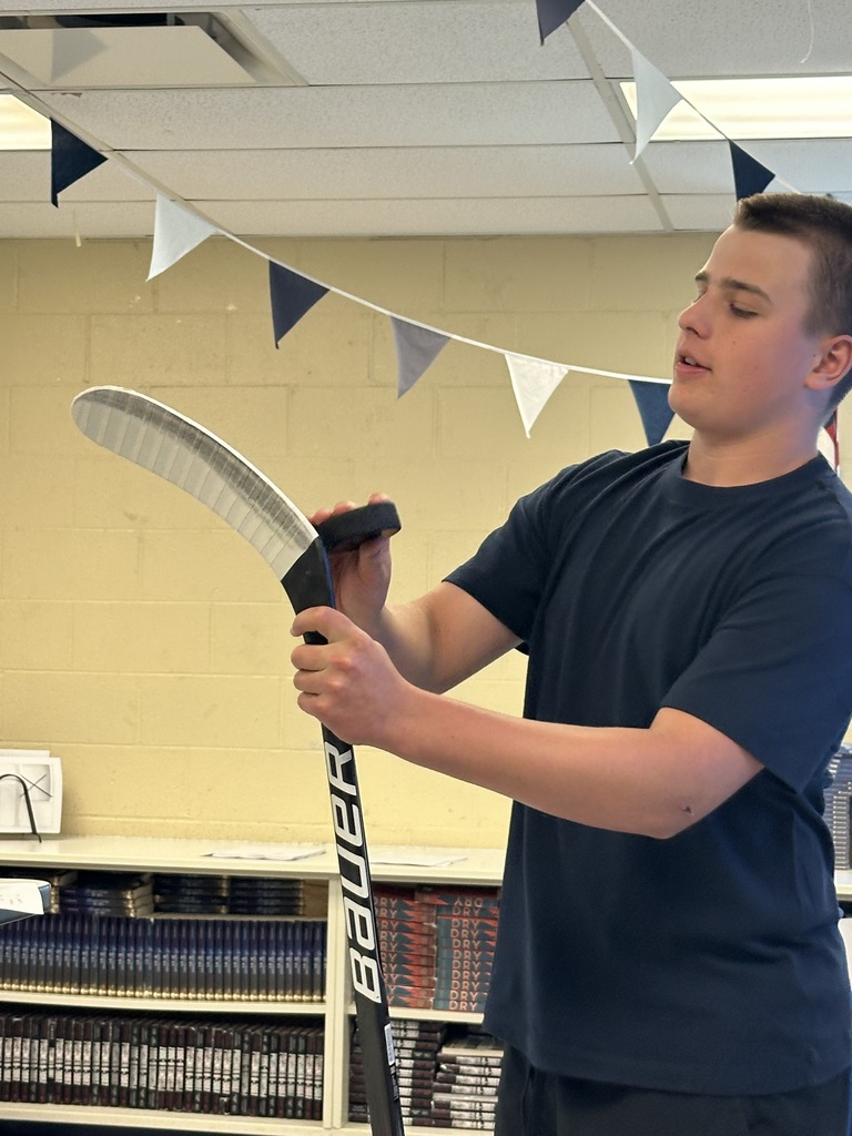 A student is standing with a hockey stick upright and demonstrating how to tape it