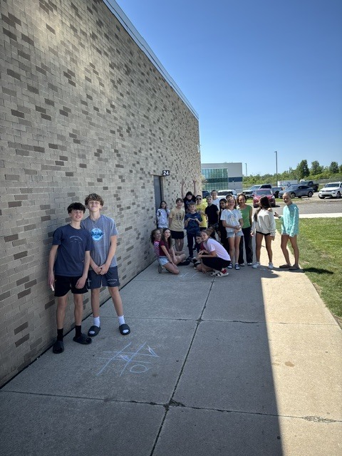 Students are posing with their sidewalk chalk creations against the school building