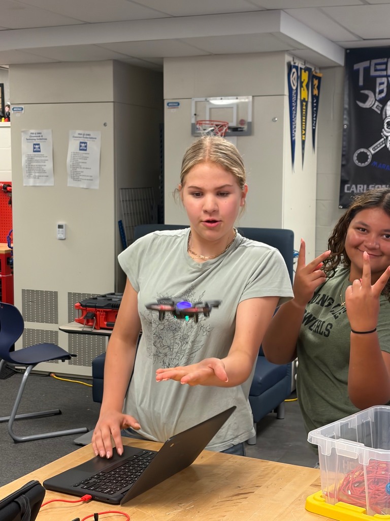 A student is looking at a drone that is hovering over her hand