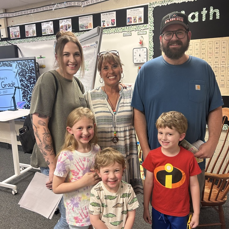 teacher posing with student and their family in classroom 