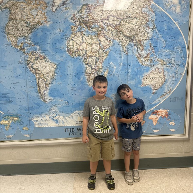 two students smiling in hallway in front of globe hung up in hallway