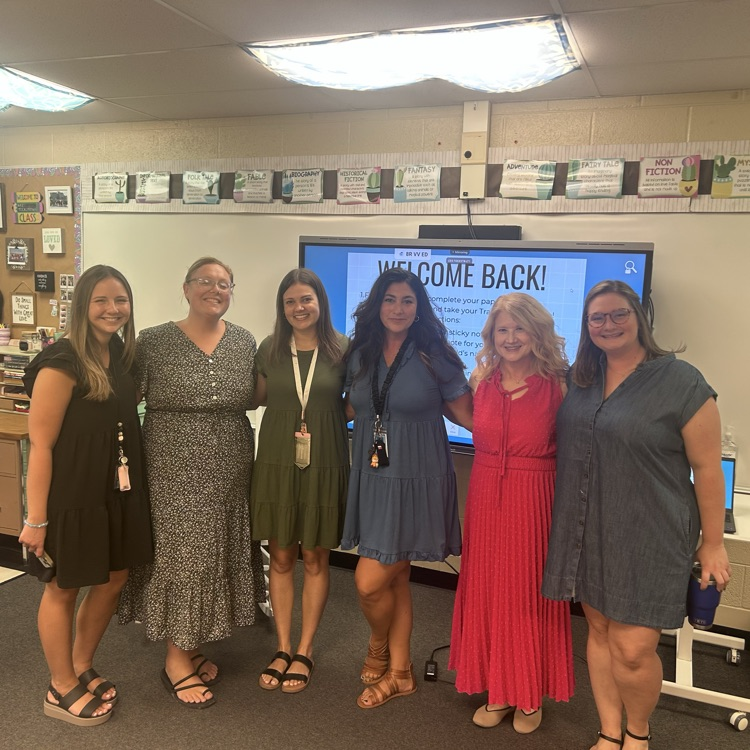 group of teachers smiling for group photo in classroom during open house 