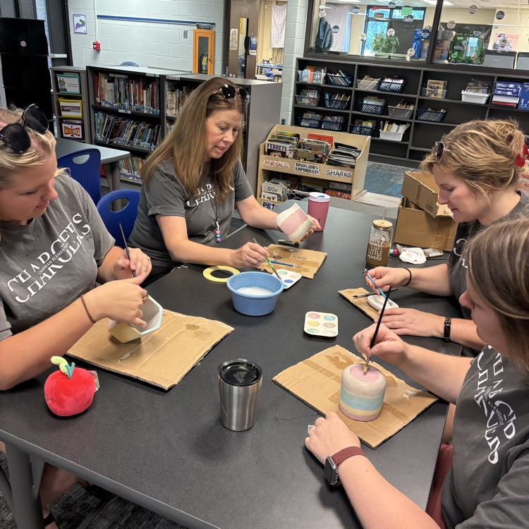 teachers sitting at table painting pottery together