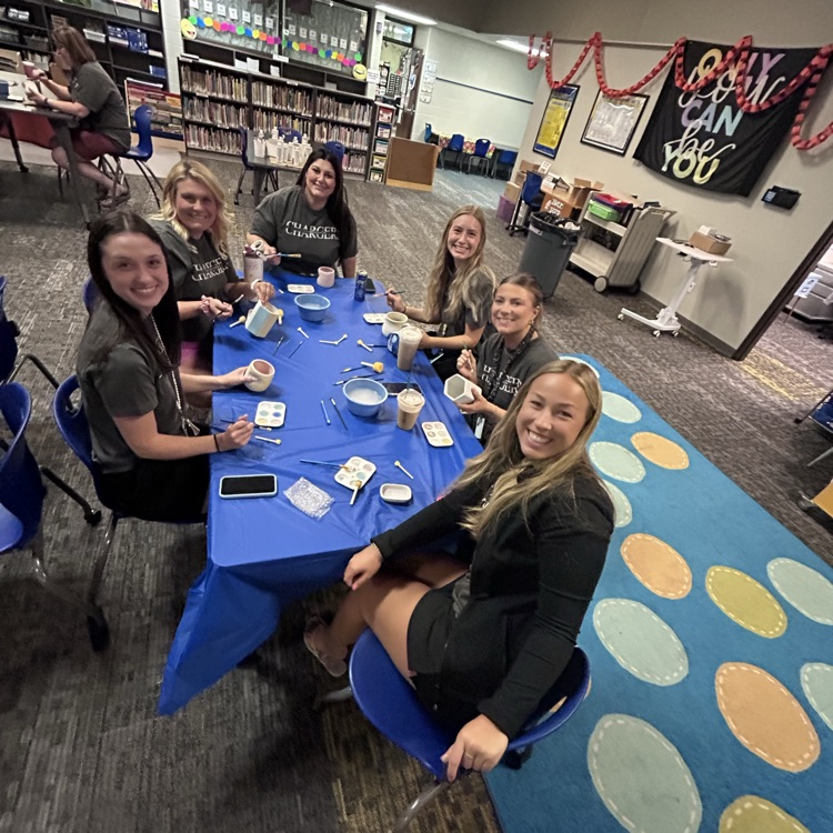 teachers sitting at table smiling at camera painting pottery together