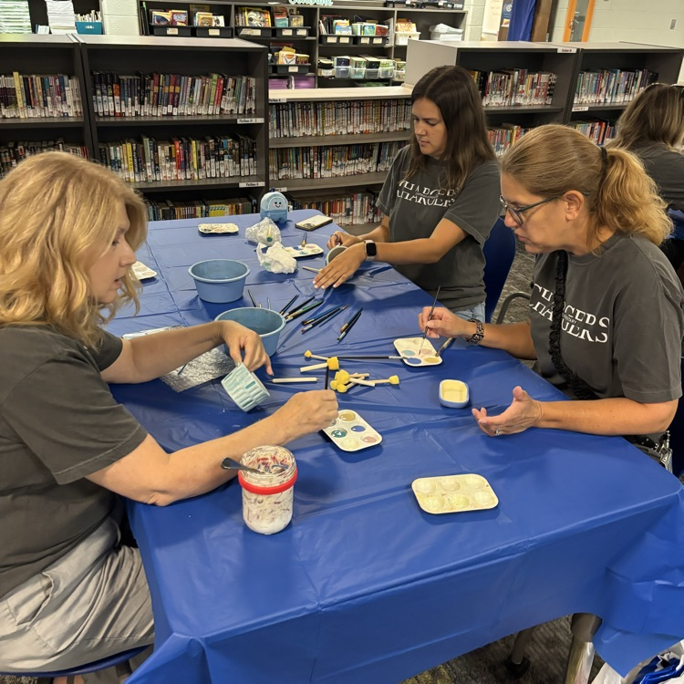 teachers sitting at table painting pottery together