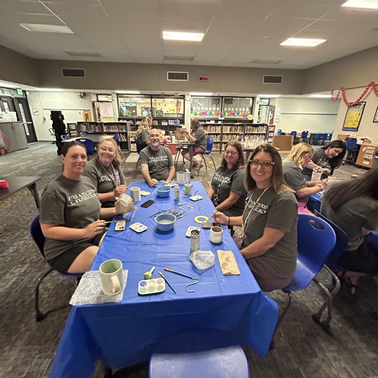 teachers sitting at table smiling at camera painting pottery together