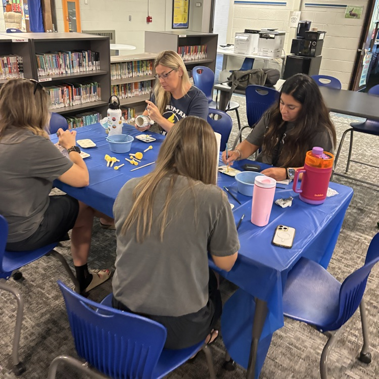 teachers sitting at table painting pottery together