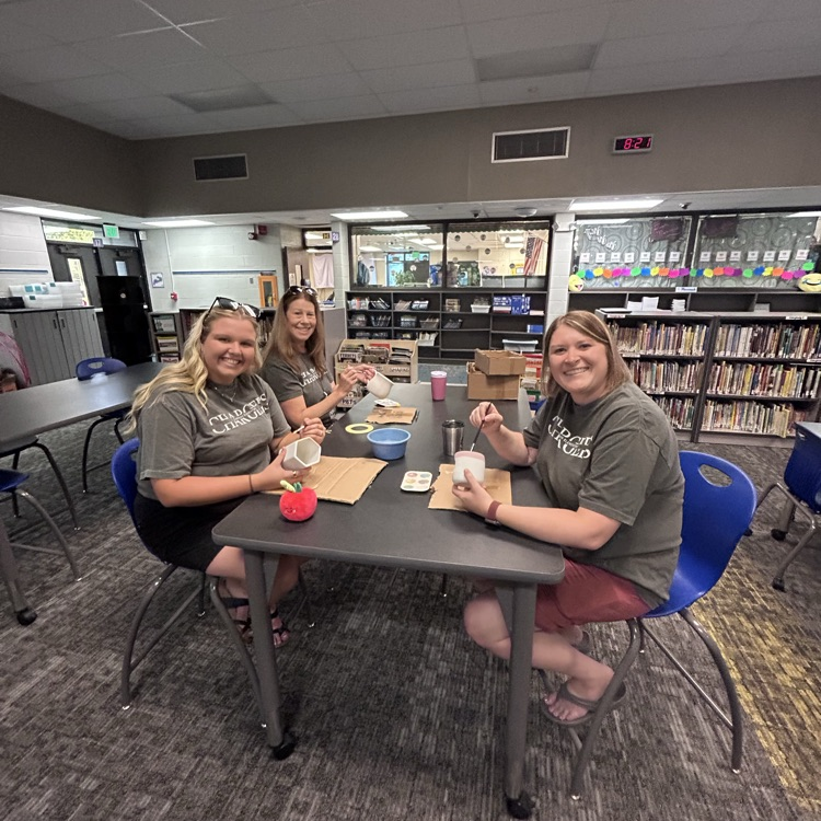 teachers sitting at table smiling at camera painting pottery together