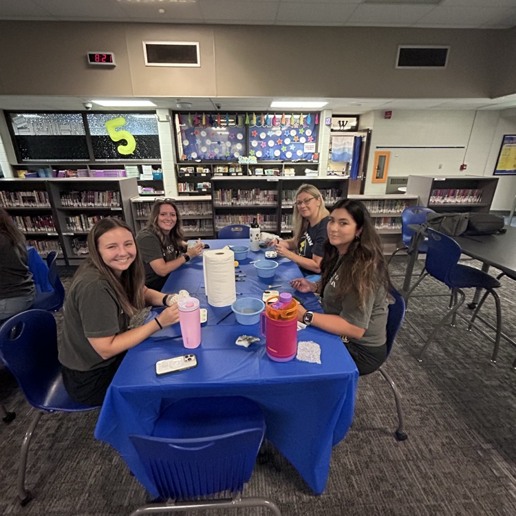 teachers sitting at table smiling at camera painting pottery together