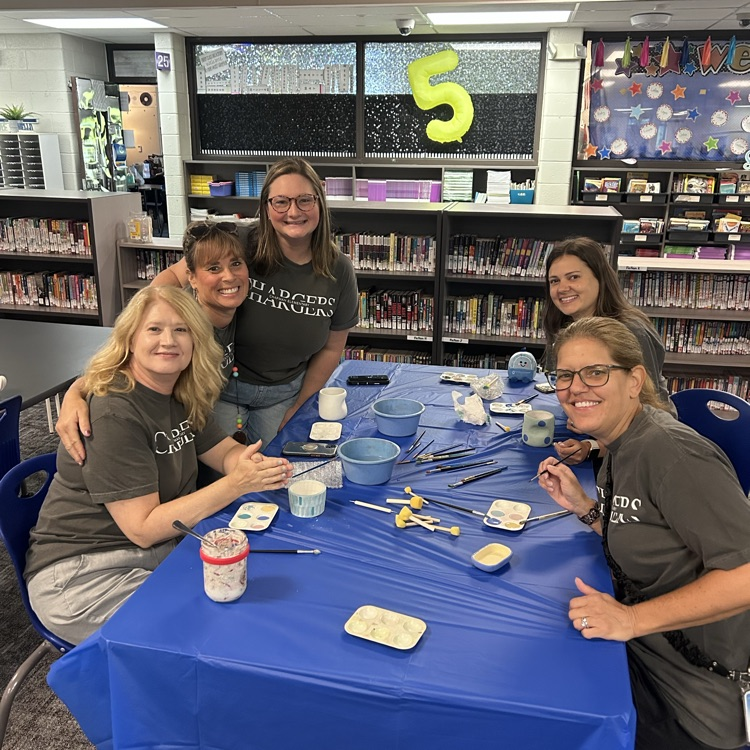 teachers sitting at table smiling at camera painting pottery together