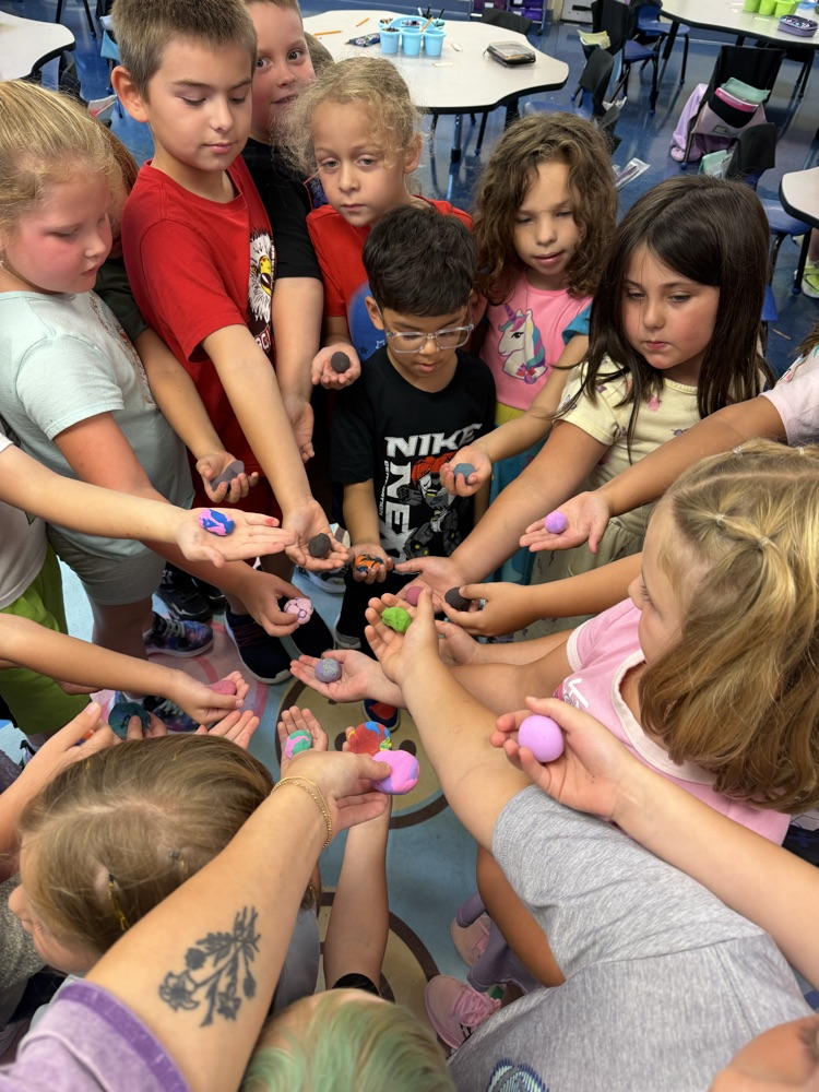 First grade students gather together, holding their colorful clay worry stones in their hands after creating them.