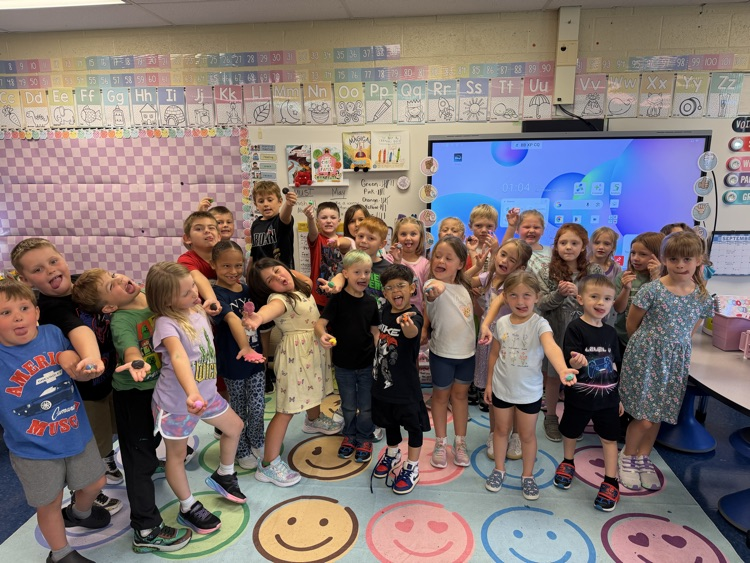 A first grade class poses together in their classroom, proudly showing off their colorful clay worry stones.