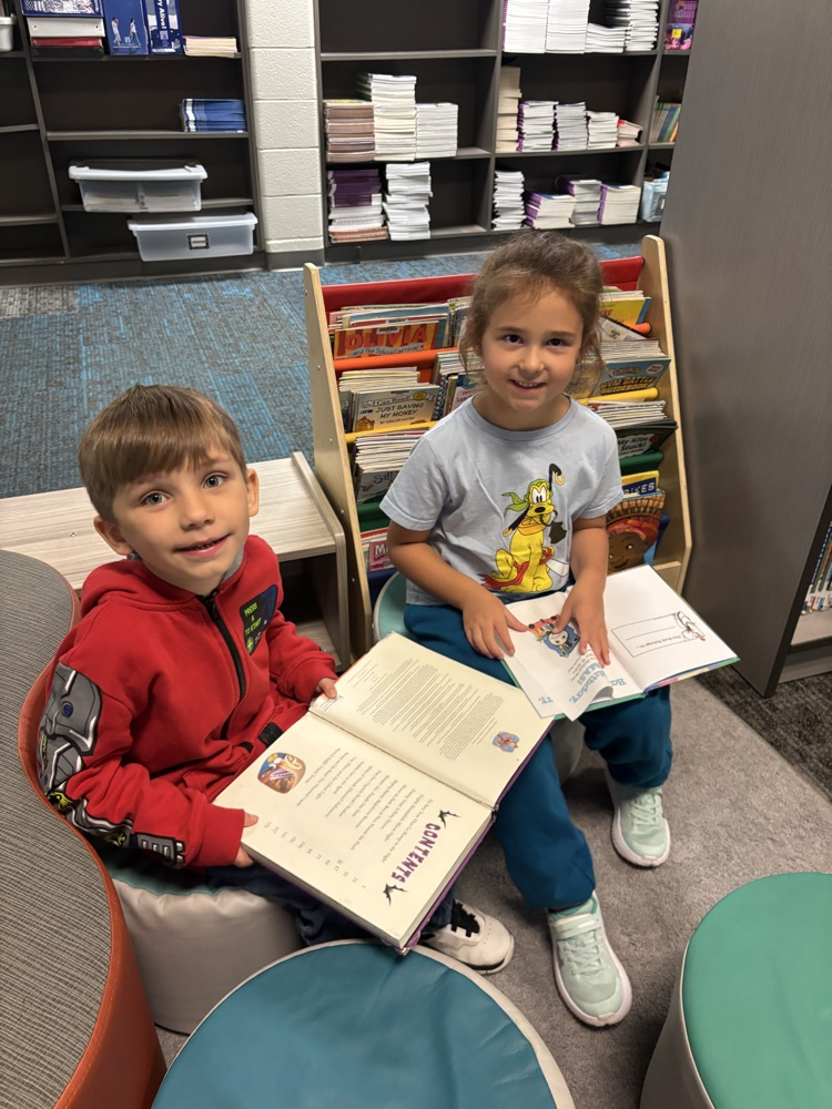 Kindergarten students from Ms. Brodeur’s class smile while holding and reading books during their first visit to the school library.