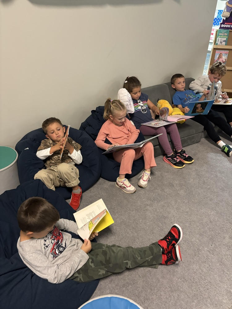 Kindergarten students from Ms. Brodeur’s class smile while holding and reading books during their first visit to the school library.