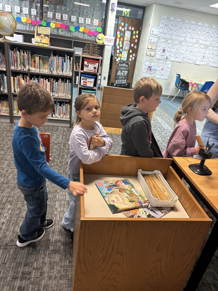 Kindergarten students from Ms. Brodeur’s class smile while holding and reading books during their first visit to the school library.