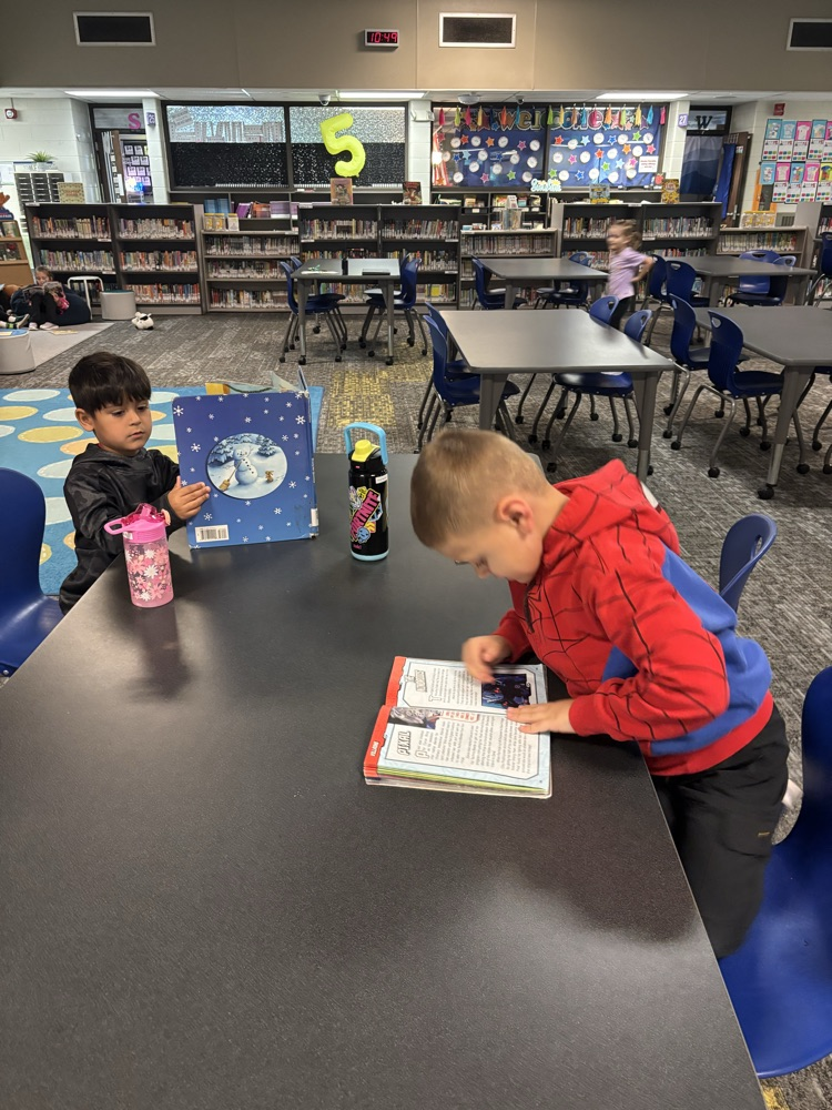 Kindergarten students from Ms. Brodeur’s class smile while holding and reading books during their first visit to the school library.