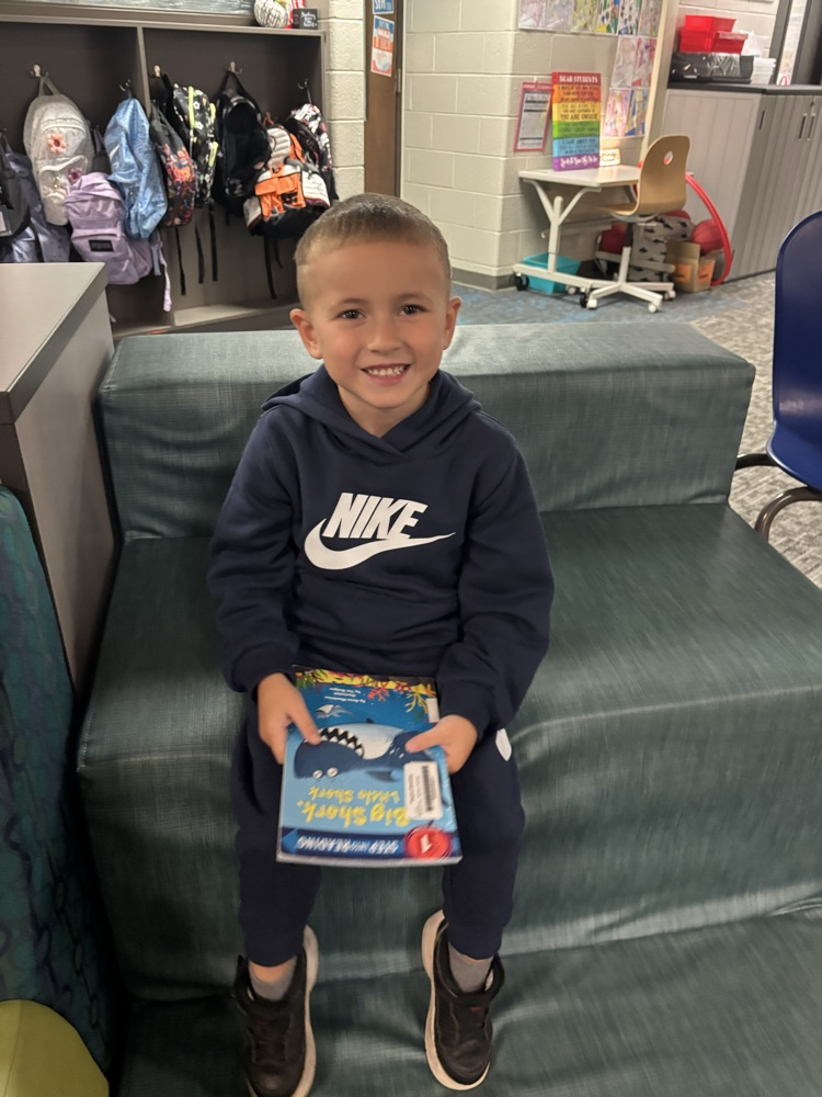 Kindergarten students from Ms. Brodeur’s class smile while holding and reading books during their first visit to the school library.