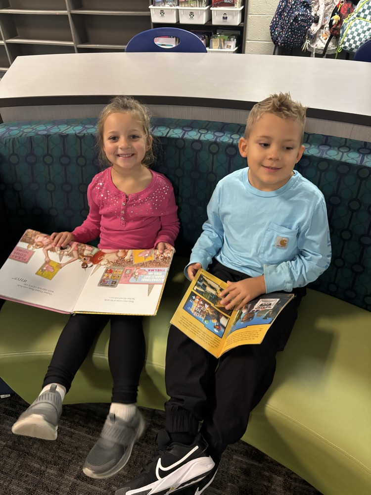 Kindergarten students from Ms. Brodeur’s class smile while holding and reading books during their first visit to the school library.