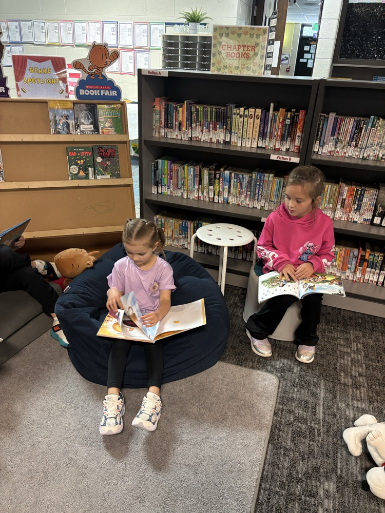 Kindergarten students from Ms. Brodeur’s class smile while holding and reading books during their first visit to the school library.