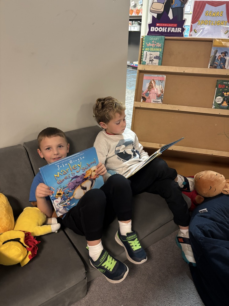 Kindergarten students from Ms. Brodeur’s class smile while holding and reading books during their first visit to the school library.