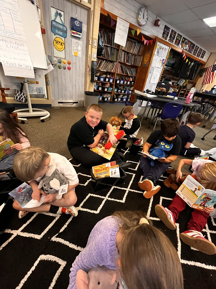 Photos show Mrs. Patrone’s 2nd grade students sitting in the classroom reading books while holding their stuffed animal buddies. Students are smiling and engaged with their books.
