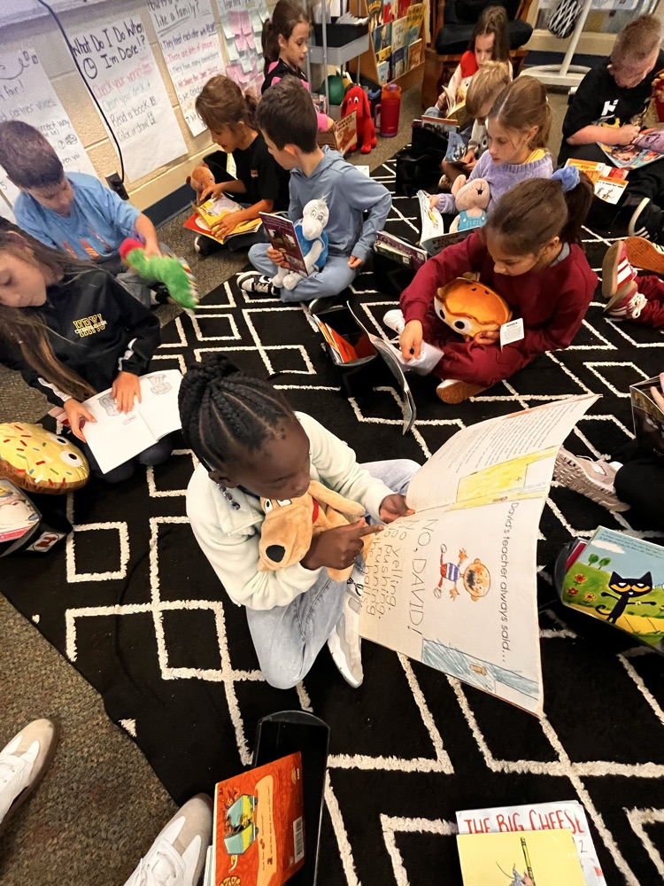 Photos show Mrs. Patrone’s 2nd grade students sitting in the classroom reading books while holding their stuffed animal buddies. Students are smiling and engaged with their books.