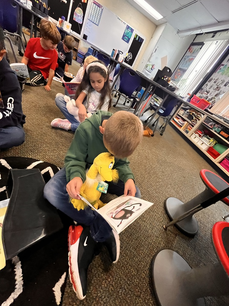 Photos show Mrs. Patrone’s 2nd grade students sitting in the classroom reading books while holding their stuffed animal buddies. Students are smiling and engaged with their books.