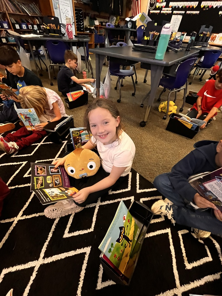 Photos show Mrs. Patrone’s 2nd grade students sitting in the classroom reading books while holding their stuffed animal buddies. Students are smiling and engaged with their books.