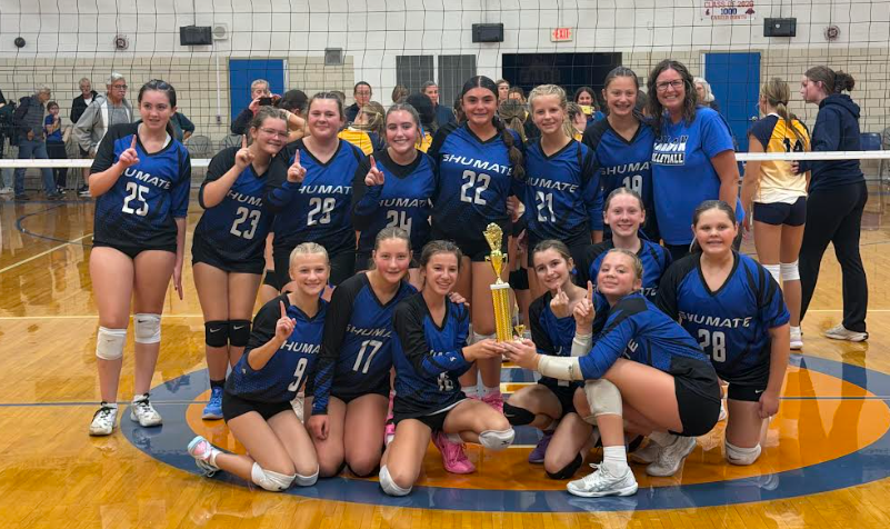 The Shumate volleyball team poses in front of the net holding the first place trophy