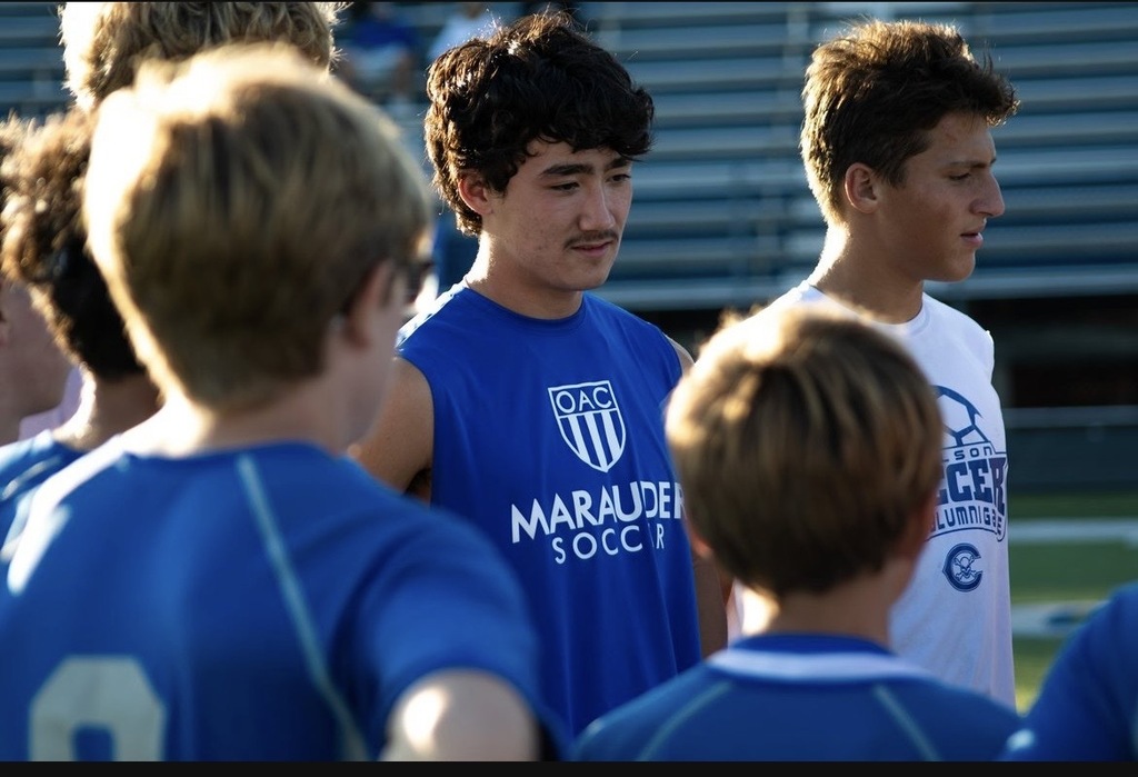 A group of boys are standing in a semi-circle at a Soccer game wearing Marauder Soccer shirts in blue and white