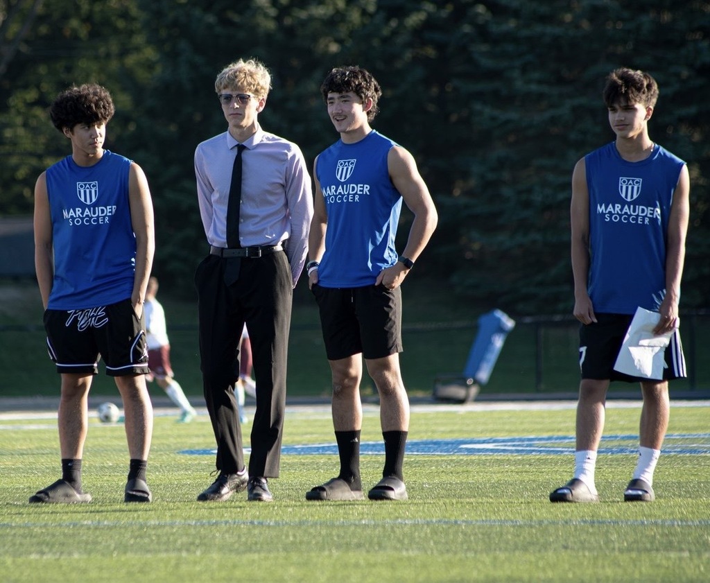 Four boys are on the sideline at a Soccer game coaching