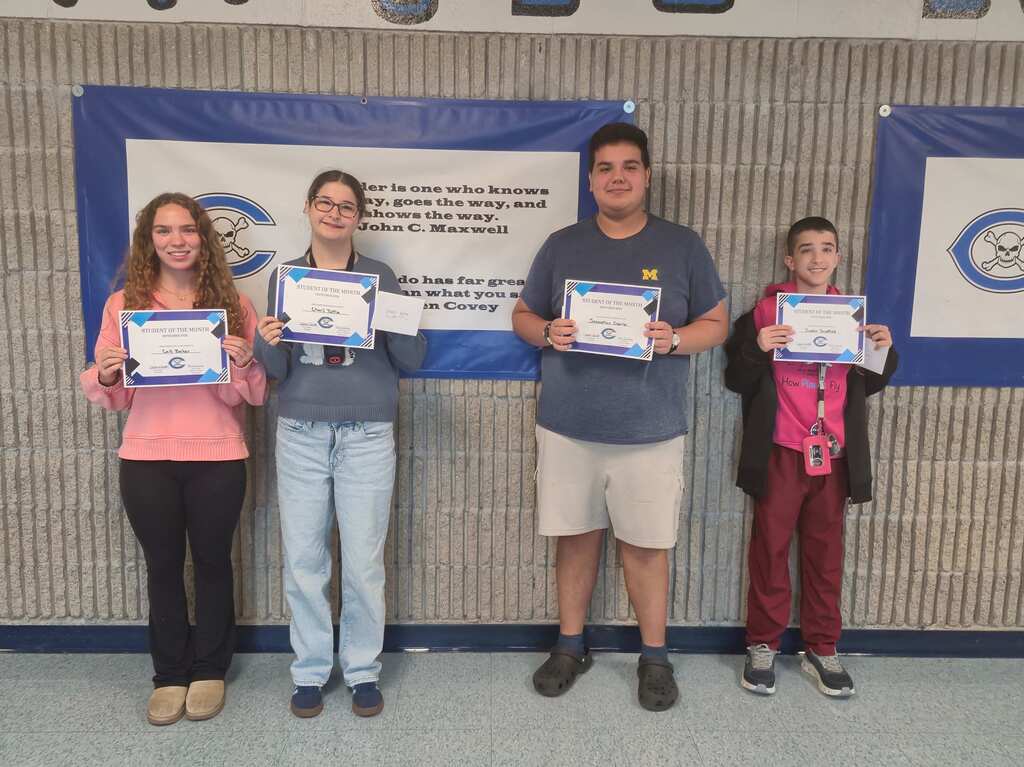 Two female and two male students with awards in front of a wall