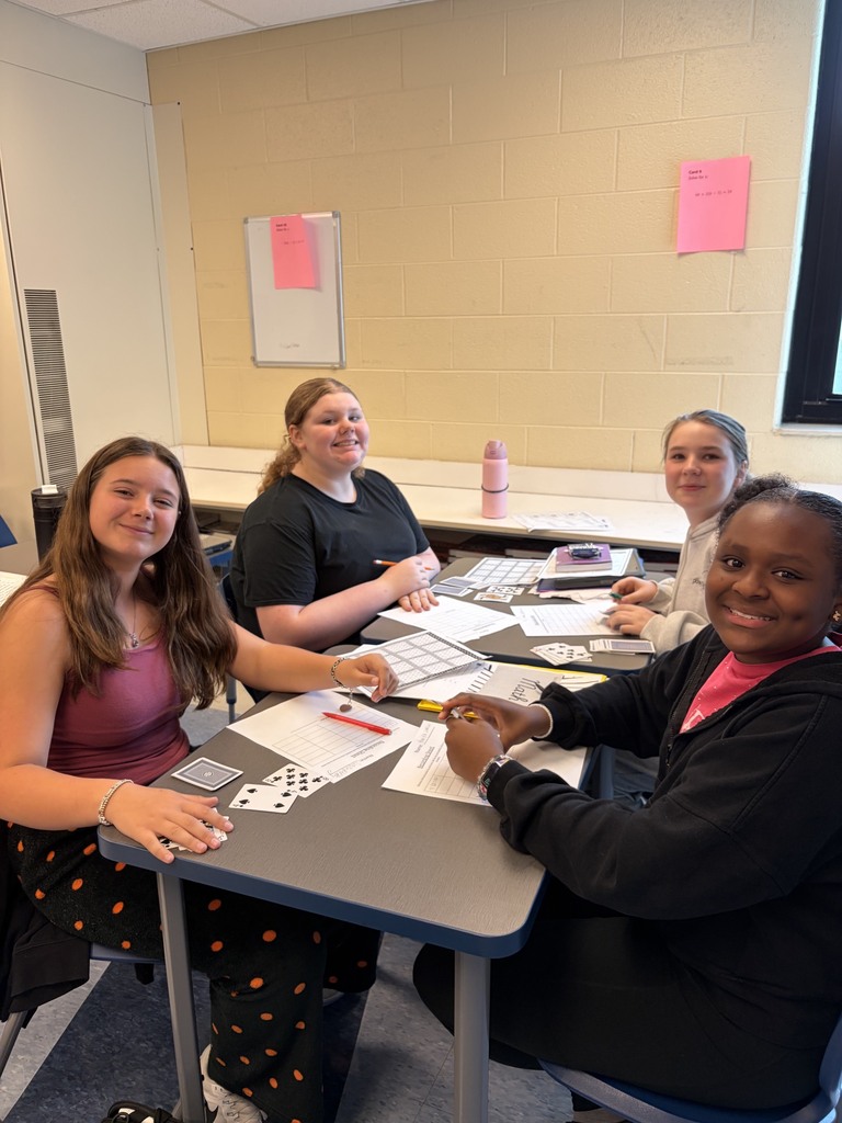 Four students sit at a table and play an integer war with cards.