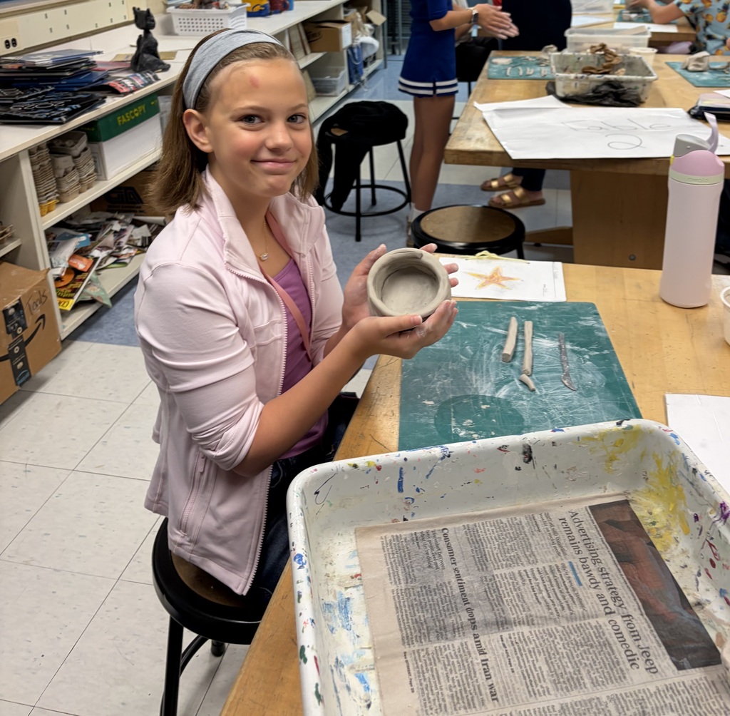 A female student holds up her clay project and smiles for the camera