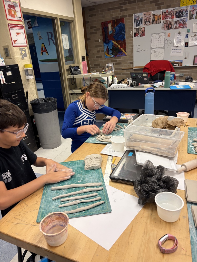 Two students sit at a table working on their clay projects surrounded by tools for making clay art