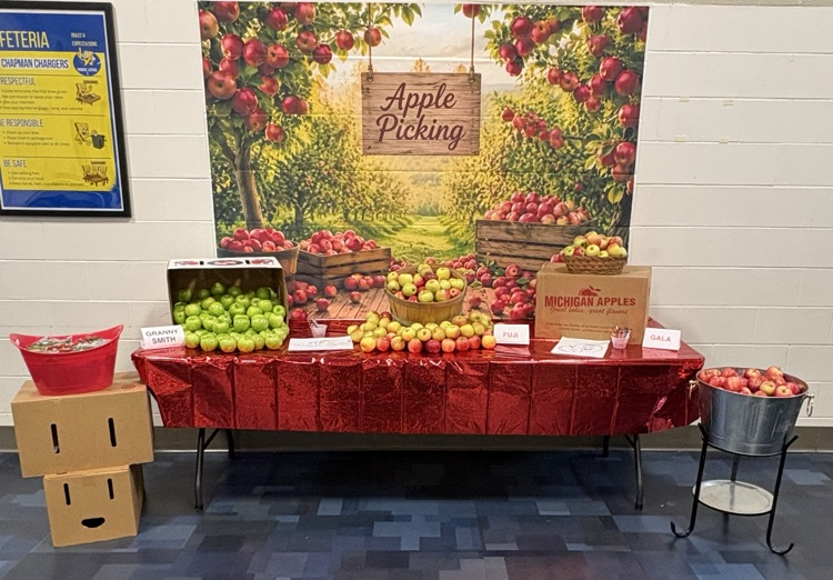 Kitchen staff and students pose by a fun apple-picking display in the cafeteria to celebrate Michigan Apple Crunch Day.