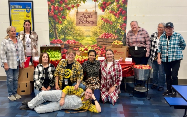 Kitchen staff and students pose by a fun apple-picking display in the cafeteria to celebrate Michigan Apple Crunch Day.