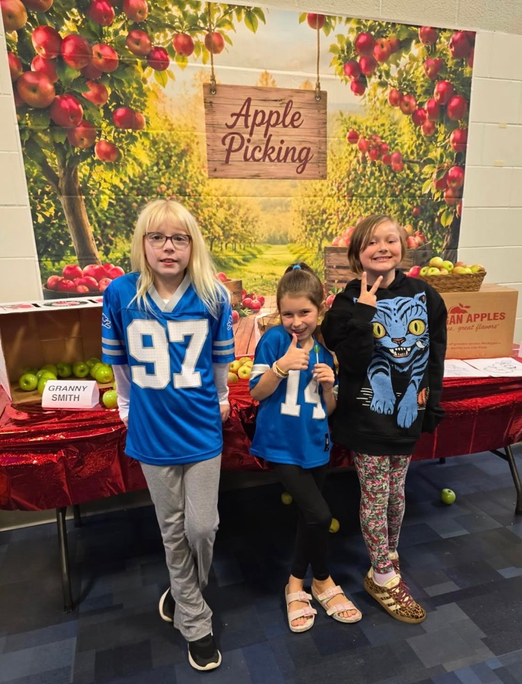 Kitchen staff and students pose by a fun apple-picking display in the cafeteria to celebrate Michigan Apple Crunch Day.