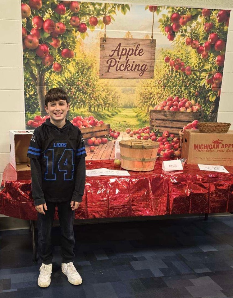 Kitchen staff and students pose by a fun apple-picking display in the cafeteria to celebrate Michigan Apple Crunch Day.