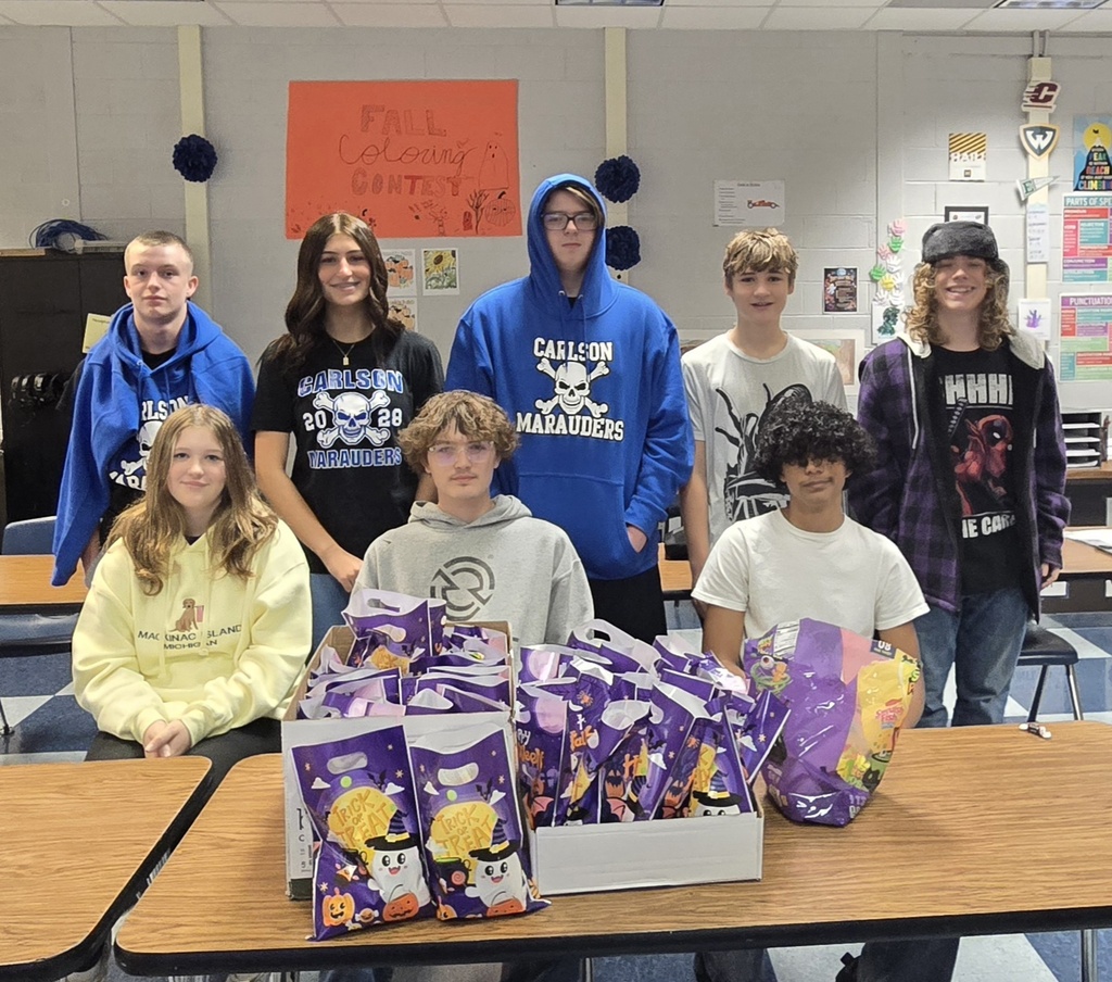 Eight students sitting in front of a pile of Halloween treat bags. 