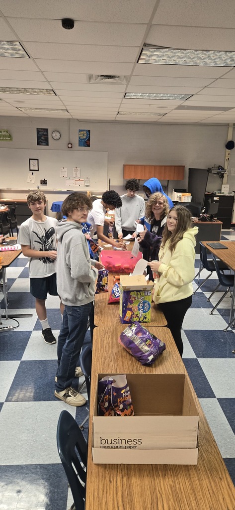 Several students standing along both sides of a table packing candy in Halloween bags like an assembly line. 