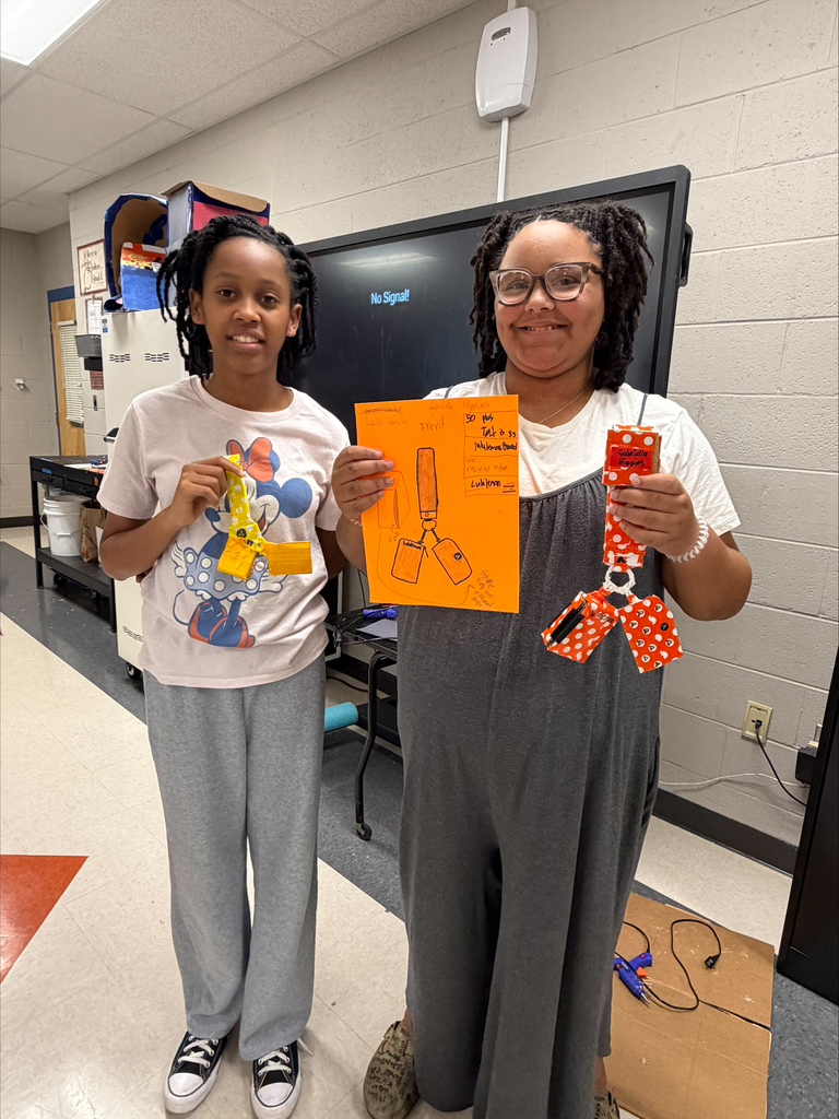 Two middle school students proudly display their colorful, handmade creations and design plans during a hands-on STEM activity.