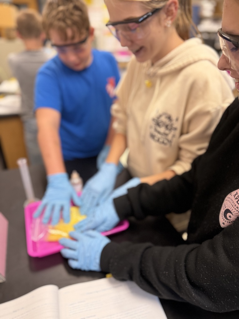 three students work together to press a material into a plastic bag