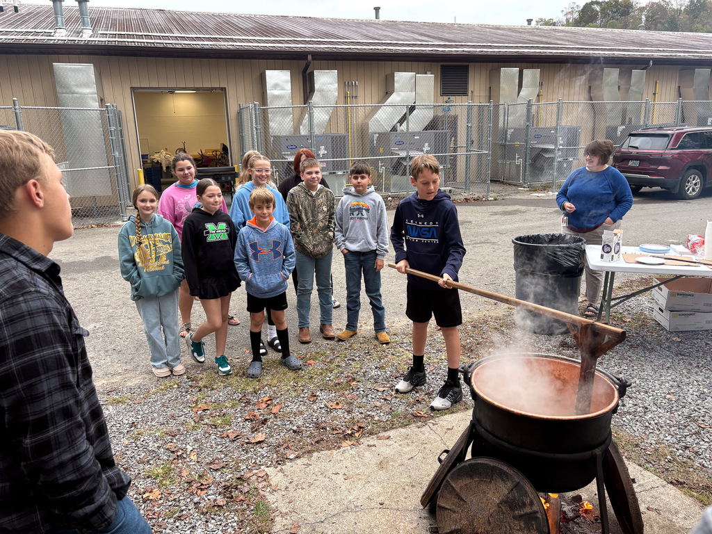 Students using a wooden pole to stir apple butter
