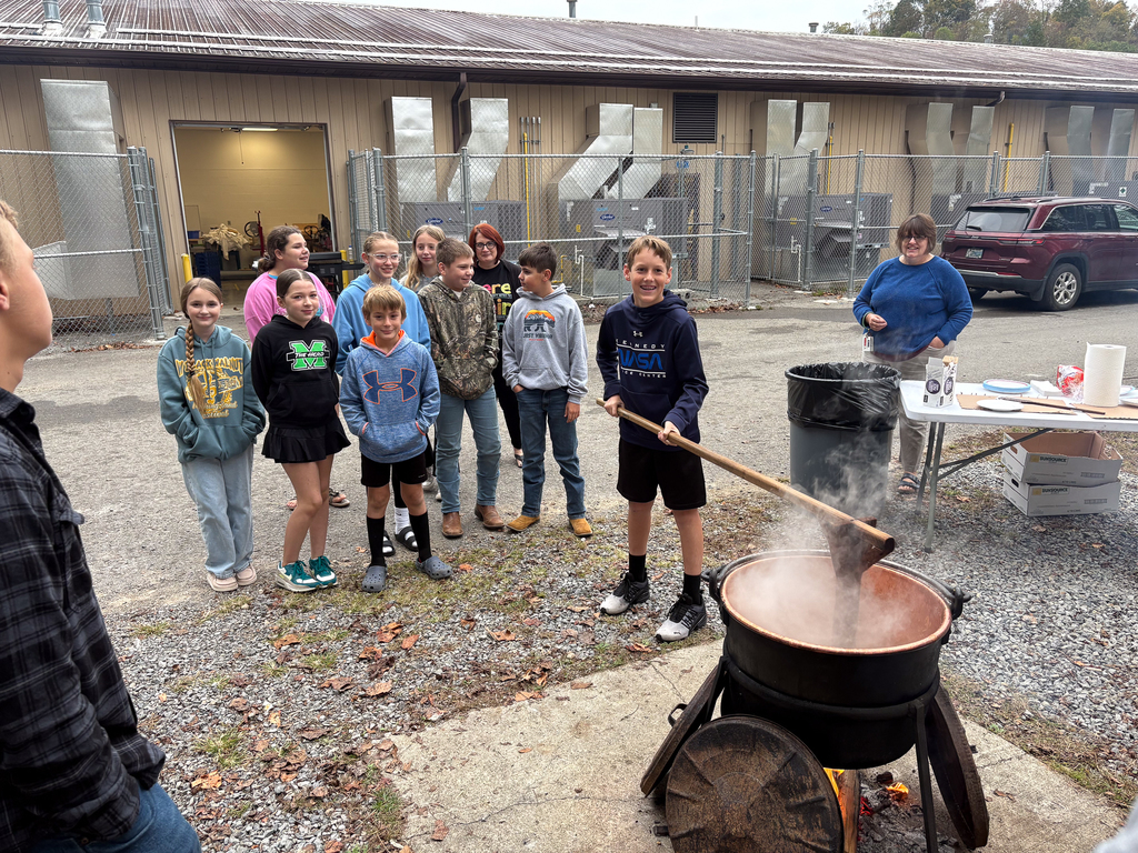 Students using a wooden pole to stir apple butter